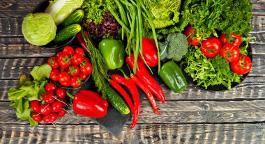 Lahana, biber, domates, salatalık, marul, vişneli domates, brokoli, siyah arkaplanda roka. Tahta bir masadaki yığının üzerinde çeşitli sebzeler.