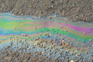 Islak asfaltta yağ lekeleri var. Su birikintileri çok renkli petrol akıntılarıyla kirlenmiş. Çevre kirliliği, petrol sızıntıları ve çevre sorunları kavramı.