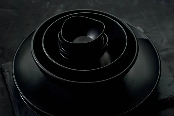 深色背景下的黑色餐具 不同形状和尺寸的盘子和碗堆在一起 对比戏剧性的光作为一种艺术效果 — 图库照片