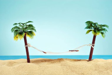 Yapay palmiye ağaçlarında minyatür hamak. Kumsalın manzarası, kumsalda palmiye ağaçları var. Arka planda mavi gökyüzü. Dinlenme ve seyahat konsepti.