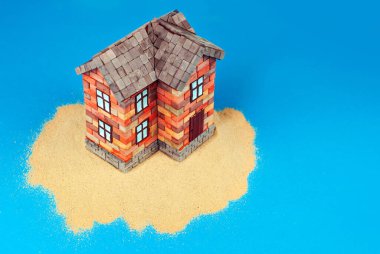 Kumda bir ev maketi. Deniz ve mavi gökyüzünün arka planında bir sahil evi. Ev ve ipotek konsepti. Cennet adasında bir ev.