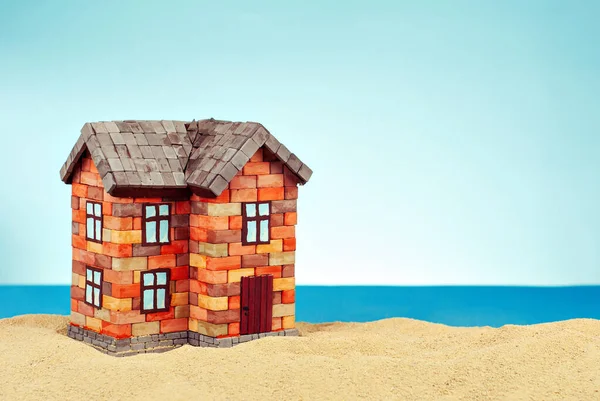 Kumda bir ev maketi. Deniz ve mavi gökyüzünün arka planında bir sahil evi. Ev ve ipotek konsepti. Evin yakınındaki cennet adası..
