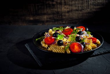 Domatesli salata, biber, ton balığı ve makarna. Siyah tabakta, siyah arka planda taze salata. Yemek yakınındaki metin için boşluk ve boş alanı kopyala.