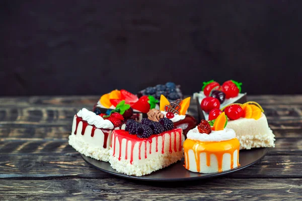 一组不同的蛋糕在黑色背景上 有巧克力和果冻的蛋糕片 红木桌子上的糖果 — 图库照片