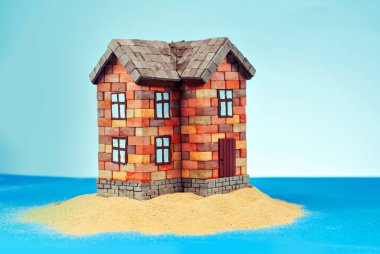 Kumda bir ev maketi. Deniz ve mavi gökyüzünün arka planında bir sahil evi. Ev ve ipotek konsepti. Cennet adasında bir ev.