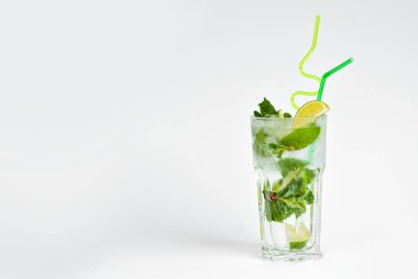 Beyaz arka planda yeşil kokteyl. Buzlu alkollü mojito. Limon, nane ve saman karışımı. Cam kenarındaki metin için yer ve şarap mekanını kopyala.