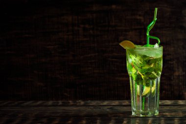 Siyah arka planda pipetli, buzlu ve meyveli kokteyl. Eski ahşap bir masada Mojito. Yakın plan. Cama yakın metin için boşluk ve boş alanı kopyala