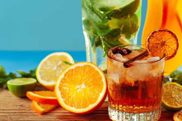 Tahtada turuncu ve yeşil kokteyller. Alkollü içecek, buz, portakal, nane ve kumda limon. Arka planda gün batımı, deniz ve gökyüzü. Meyveyle farklı içeceklerin karışımı..