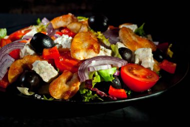 Domatesli salata, biber, zeytin ve tavuk filetosu. Siyah bir tabakta siyah bir arka planda taze salata..