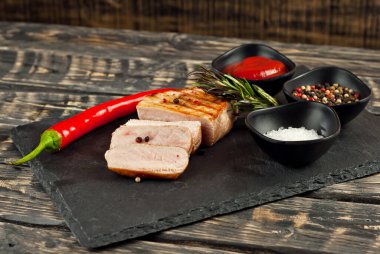 Kesme tahtasında dilimlenmiş domatesli biftek. Koyu ahşap arka planda et. Yemek, sos, tuz, biber ve baharatlar eski püskü bir masada..