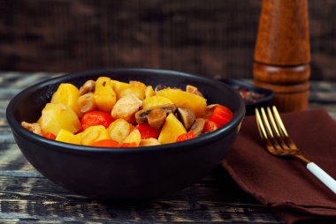 Siyah kasede etli haşlanmış patates. Mantarlı ve havuçlu patates. Haşlanmış mantar ve patatesli tavuk. Siyah ahşap bir masada yemek. 