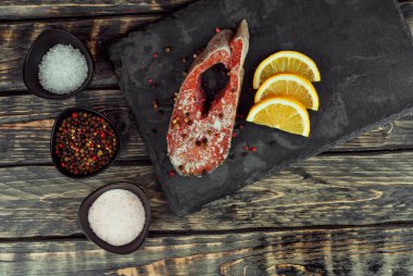 Siyah bir tabakta çiğ somon bifteği. Limonlu kırmızı somon. Sefil ahşap masada yemek..