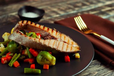 Izgara somon bifteği. Limonlu ve sebzeli kırmızı somon. Haşlanmış lahana, havuç, bezelye ve brokoli salatası. Sefil ahşap masada yemek..