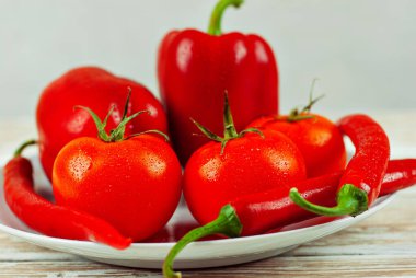 Beyaz arka planda biberler ve domatesler. Kapalı tabakta kırmızı sebzeler. Eski püskü bir tahtada acı biber ve domates. 