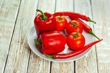 Beyaz arka planda biberler ve domatesler. Kapalı tabakta kırmızı sebzeler. Eski püskü bir tahtada acı biber ve domates. 