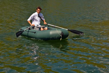 Şişme teknede beyaz gömlekli bir adam. Göl kenarında dizüstü bilgisayarı olan bir iş adamı. Uzaktan çalışma, boş zaman ve serbest çalışma kavramı..