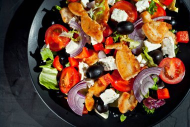 Domatesli salata, biber, zeytin ve tavuk filetosu. Siyah bir tabakta siyah bir arka planda taze salata..