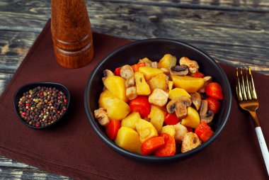 Siyah kasede etli haşlanmış patates. Mantarlı ve havuçlu patates. Haşlanmış mantar ve patatesli tavuk. Siyah ahşap bir masada yemek. 