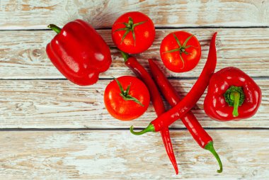 Beyaz arka planda biberler ve domatesler. Kırmızı sebzeler yakın. Eski püskü bir tahtada acı biber ve domates. 