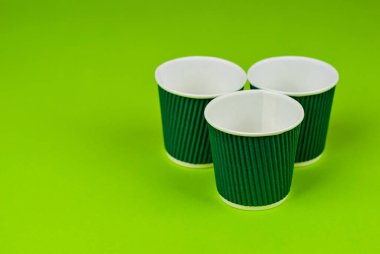 Yeşil arka planda tek kullanımlık kağıt bardaklar. Ekolojik kahve tabakları. Gözlük yakınındaki metin için boşluk ve boş alanı kopyala.