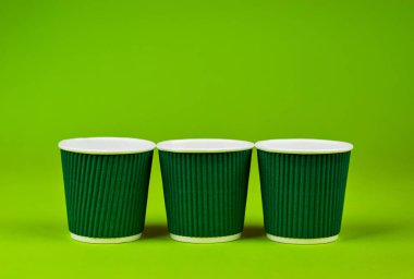 Yeşil arka planda tek kullanımlık kağıt bardaklar. Ekolojik kahve tabakları. Gözlük yakınındaki metin için boşluk ve boş alanı kopyala.