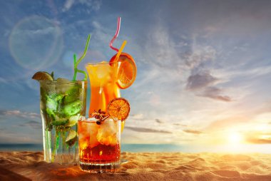 Plajda turuncu ve yeşil kokteyller. Buzlu, portakallı, naneli ve limonlu alkollü içecek. Arka planda gün batımı, deniz ve gökyüzü. Cama yakın metin için boşluk ve boş alanı kopyala.