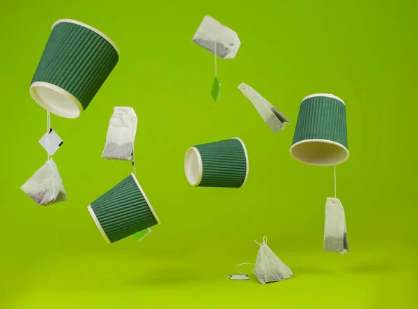 Disposable cardboard cups and tea bags fly in the air. Paper cups on a green background.