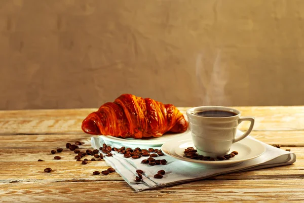 白いセラミックマグカップでコーヒー 朝食はコーヒーとクロワッサン 古い木製のテーブルの上のコーヒー マグカップの近くにコーヒー豆が散乱している — ストック写真