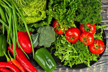 Lahana, biber, domates, salatalık, marul, vişneli domates, brokoli, siyah arkaplanda roka. Tahta bir masadaki yığının üzerinde çeşitli sebzeler.