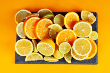 Portakallar, limonlar ve dilimlenmiş limonlar. Turuncu arka planda turuncu sebzeler. Meyve suyu ve kokteyl için sebze hazırlıyorum..