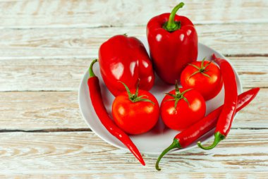 Beyaz arka planda biberler ve domatesler. Kapalı tabakta kırmızı sebzeler. Eski püskü bir tahtada acı biber ve domates. Yemek yakınındaki metin için boşluk ve boş alanı kopyala.
