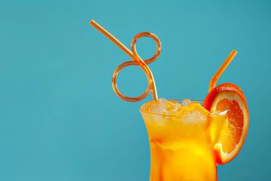 Turuncu kokteyl ve pipetler. Buzlu alkollü içecek, mavi arka planda turuncu..