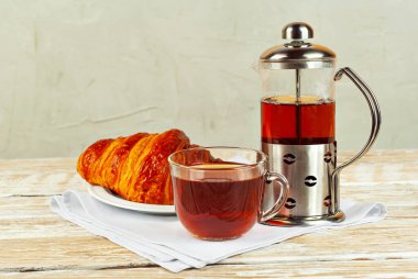 Beyaz tabakta kruvasan ve çay. Eski ahşap bir masada çay fincanı. Sarı ahşap bir tahtanın üzerinde çay ile kahvaltı. Yemek yakınındaki metin için boşluk ve boş alanı kopyala.