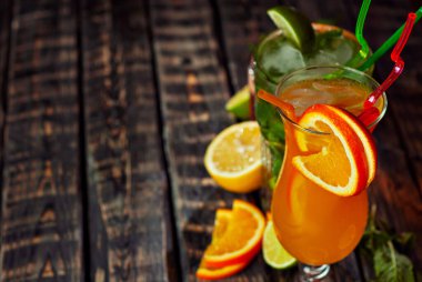 Siyah arka planda pipetli, buzlu ve meyveli kokteyller. Eski ahşap bir masada alkollü içecekler. Yakın plan. Eski püskü kahverengi bir tahtanın üzerinde iç. Cama yakın metin için boşluk ve boş alanı kopyala.