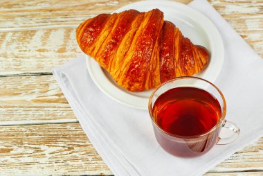 Beyaz tabakta kruvasan ve çay. Eski ahşap bir masada çay fincanı. Sarı ahşap bir tahtanın üzerinde çay ile kahvaltı. Yemek yakınındaki metin için boşluk ve boş alanı kopyala.
