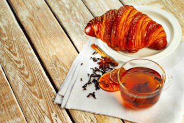 Beyaz tabakta kruvasan ve çay. Eski ahşap bir masada çay fincanı. Tam yaprak siyah çay, limon ve tarçınlı peçete. Yemek yakınındaki metin için boşluk ve boş alanı kopyala.