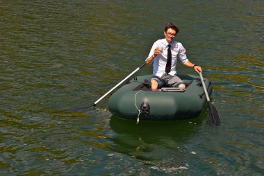 Şişme teknede beyaz gömlekli bir adam. Göl kenarında dizüstü bilgisayarı olan bir iş adamı. Uzaktan çalışma, boş zaman ve serbest çalışma kavramı..