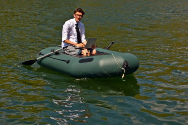 Şişme teknede beyaz gömlekli bir adam. Göl kenarında dizüstü bilgisayarı olan bir iş adamı. Uzaktan çalışma, boş zaman ve serbest çalışma kavramı..