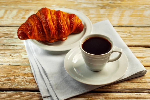 Beyaz seramik bardakta kahve. Kahvaltıda kruvasan ve kahve. Eski ahşap bir masada kahve..