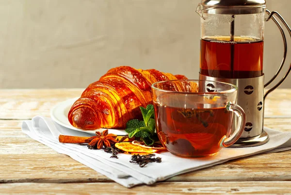 Beyaz tabakta kruvasan ve çay. Eski ahşap bir masada çay fincanı. Tam siyah çay, limon, nane yaprağı ve peçetede tarçın. Yemek yakınındaki metin için boşluk ve boş alanı kopyala.