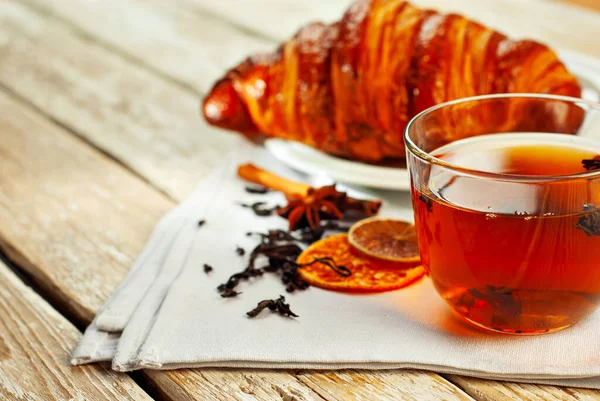 Beyaz tabakta kruvasan ve çay. Eski ahşap bir masada çay fincanı. Tam yaprak siyah çay, limon ve tarçınlı peçete. Yemek yakınındaki metin için boşluk ve boş alanı kopyala.