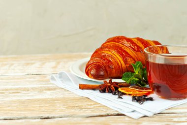 Beyaz tabakta kruvasan ve çay. Eski ahşap bir masada çay fincanı. Tam siyah çay, limon, nane yaprağı ve peçetede tarçın. Yemek yakınındaki metin için boşluk ve boş alanı kopyala.