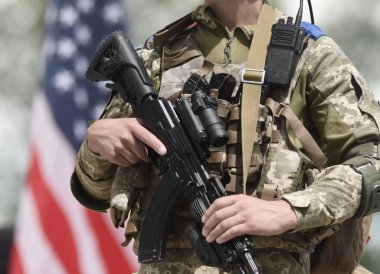 Arka planda saldırı tüfeği ve Amerikan bayrağı olan bir asker. ABD ordusu Ukrayna 'ya destek.