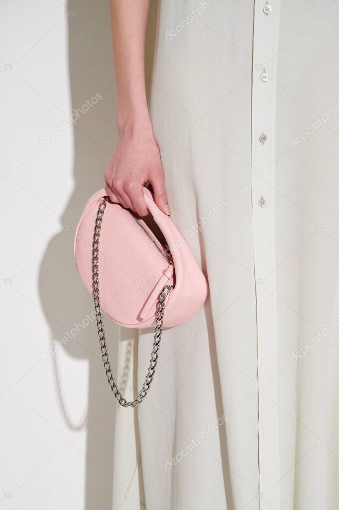 Slim girl in light dress with buttons with pink leather handbag with metal chain. Hard light. Vertical photo.