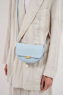 Beyaz arka planda mavi deri çantalı bej takım elbiseli bir kız. Eyer omuz çantası. Dikey fotoğraf. Yakın çekim..