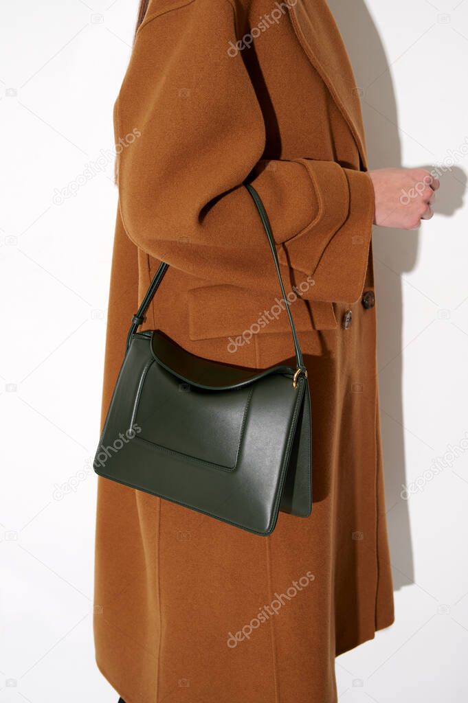 Woman in a brown  coat with luxury green leather handbag. Fashionable shoulder bag. White background. Vertical photo.