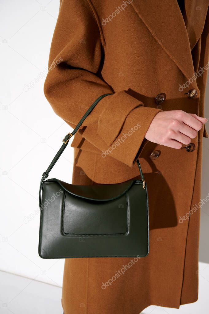 Woman in a brown  coat with luxury green leather handbag. Fashionable shoulder bag. White background. Vertical photo.