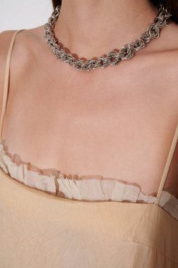 Bej elbiseli kız. Kızların boynunda kocaman gümüş bir zincir var. Kadın vücudunda lüks bir aksesuar. Küstah kalın zincir. Yakın çekim..