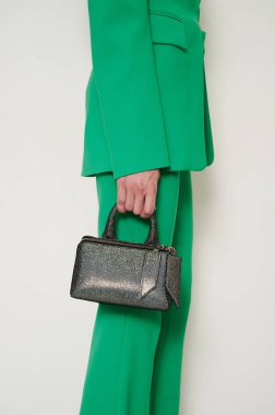 Girl in green suit with shiny black handbag in her hand. Green pants and blazer with fashionable accessory. Vertical photo.
