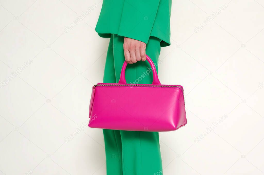Girl in green suit with pink leather handbag in her hand. Green pants and blazer with fashionable accessory. Horizontal photo with copy space. White background.